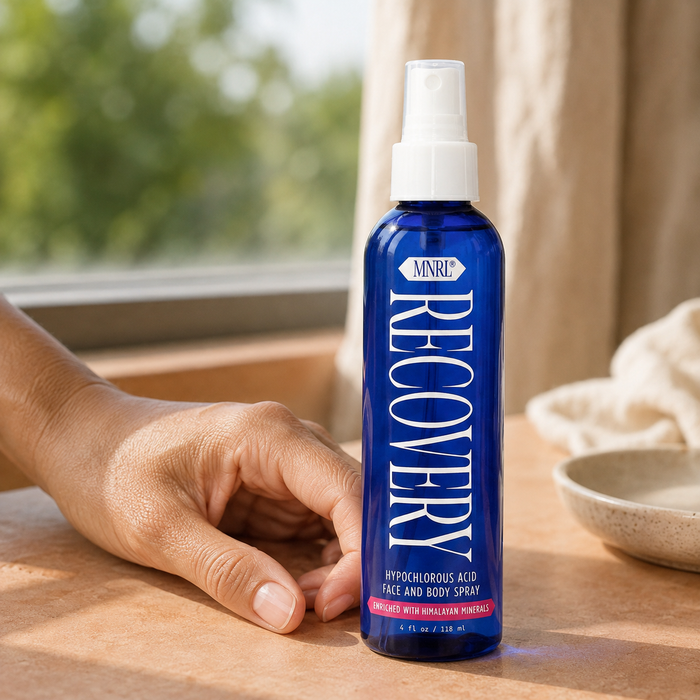 Close-up of a hand beside a bottle of MNRL Recovery hypochlorous acid spray on a table